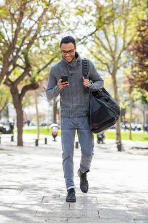 Téléchargez les photos : Portrait complet du jeune homme cool utilisant un sac de transport de téléphone portable à l'extérieur - en image libre de droit