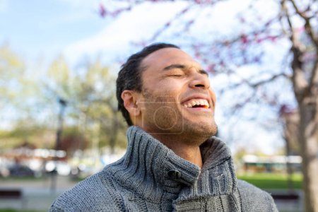 Téléchargez les photos : Gros plan portrait de joyeux jeune homme noir en pull profitant de la promenade à l'extérieur dans la ville un jour d'hiver - en image libre de droit