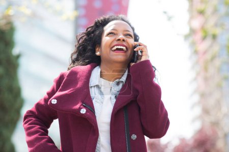 Téléchargez les photos : Portrait de femme africaine riant et parlant sur téléphone portable dans la ville - en image libre de droit