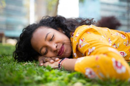 Foto de Primer plano retrato de la atractiva joven africana descansando en la hierba exterior con los ojos cerrados - Imagen libre de derechos