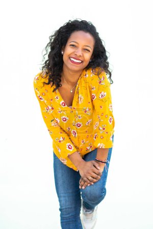 Téléchargez les photos : Portrait de jolie jeune femme noire penchée au mur blanc avec les mains sur les genoux - en image libre de droit