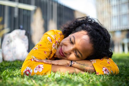 Téléchargez les photos : Gros plan portrait de jeune femme africaine reposant sur l'herbe dans le parc - en image libre de droit