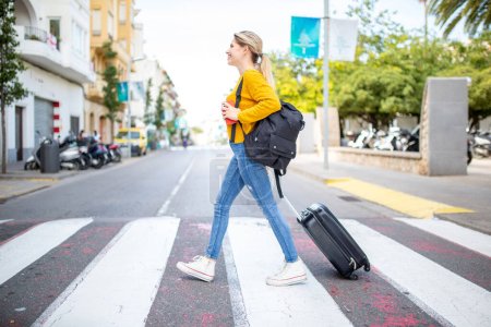 Photo for Full body side portrait of pretty young woman crossing the street with travel bag - Royalty Free Image