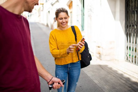 Téléchargez les photos : Jeune couple de touristes utilisant l'application de navigation sur téléphone portable tout en marchant dans une ville étrangère - en image libre de droit