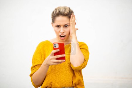 Foto de Retrato de cerca de la joven sorprendida mirando el teléfono móvil sobre fondo blanco - Imagen libre de derechos