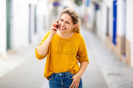 Foto de Retrato de una joven alegre hablando por celular caminando al aire libre en la ciudad - Imagen libre de derechos