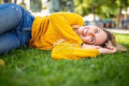 Téléchargez les photos : Portrait d'une belle jeune femme allongée sur l'herbe dehors et souriante - en image libre de droit