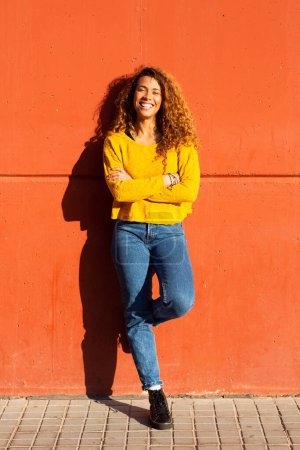 Foto de Retrato de larga duración de una hermosa joven latina apoyada en una pared naranja - Imagen libre de derechos