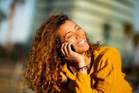 Foto de Retrato de cerca de una joven latina riéndose hablando por celular al aire libre en la ciudad - Imagen libre de derechos