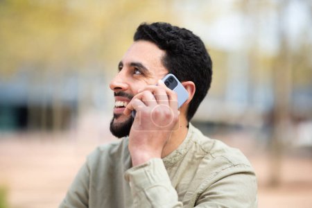 Photo for Close up portrait of happy young arabic man talking on mobile phone outside - Royalty Free Image