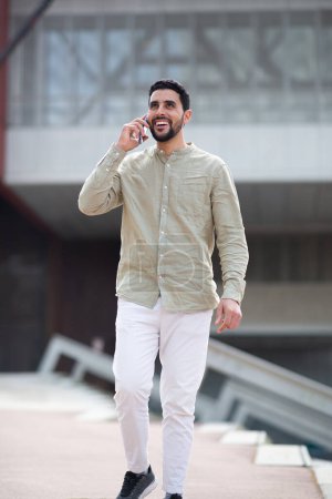 Photo for Portrait of handsome young arabic man walking and talking on mobile phone outside - Royalty Free Image