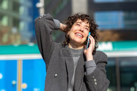 Téléchargez les photos : Portrait d'une jolie jeune femme en manteau parlant sur un téléphone portable à l'extérieur de la ville - en image libre de droit