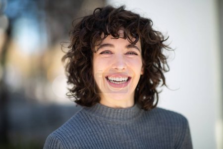 Foto de Retrato de cerca de una hermosa joven con el pelo corto mirando a la cámara y sonriendo afuera - Imagen libre de derechos