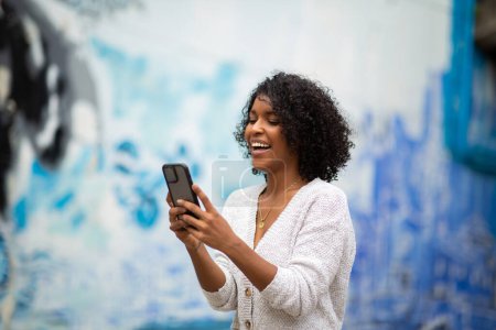Téléchargez les photos : Portrait souriant jeune femme afro-américaine utilisant un téléphone mobile - en image libre de droit