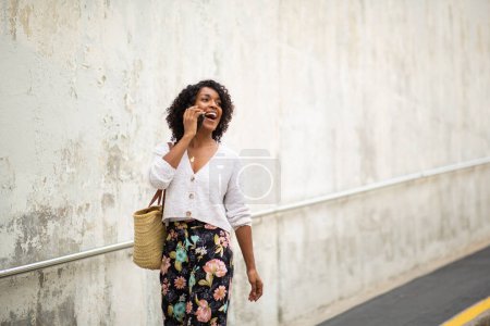 Téléchargez les photos : Portrait jeune femme afro-américaine marchant et parlant avec un téléphone portable - en image libre de droit