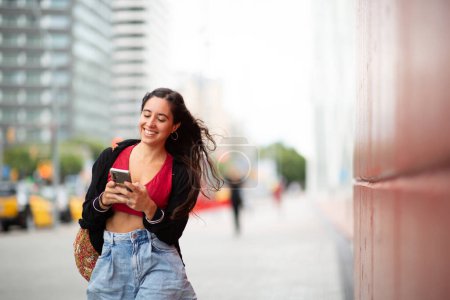Téléchargez les photos : Portrait de jeune femme souriante marchant avec un téléphone portable en ville - en image libre de droit
