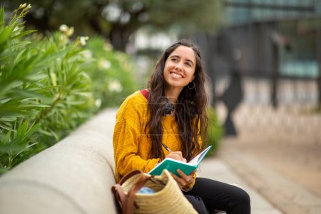 Foto de Retrato de una joven sonriente sentada con libro y pluma - Imagen libre de derechos