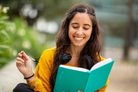 Photo for Portrait of happy young woman sitting with book and pen - Royalty Free Image