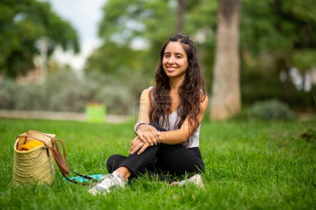 Photo for Portrait of smiling young woman sitting on grass in park - Royalty Free Image