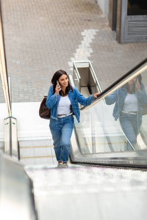 Photo for Full body portrait young woman talking with mobile phone on escalator - Royalty Free Image