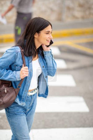 Foto de Retrato lateral mujer joven caminando con teléfono celular y bolsa - Imagen libre de derechos