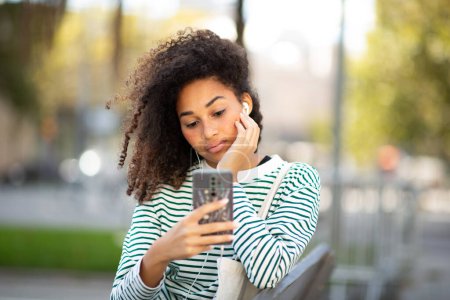 Téléchargez les photos : Portrait jeune femme assise avec téléphone portable écoutant avec des écouteurs - en image libre de droit