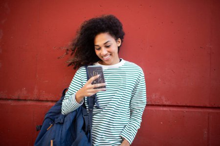Téléchargez les photos : Portrait jeune femme souriante debout au mur, regardant le téléphone mobile - en image libre de droit