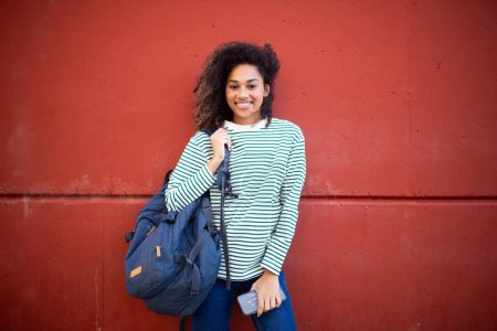 Photo for Portrait cheerful young african american woman standing by wall with school bag - Royalty Free Image