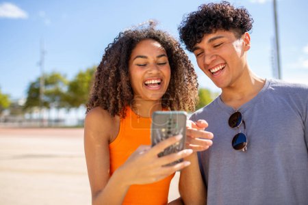 Téléchargez les photos : Portrait de jeune couple souriant regardant le téléphone mobile ensemble - en image libre de droit