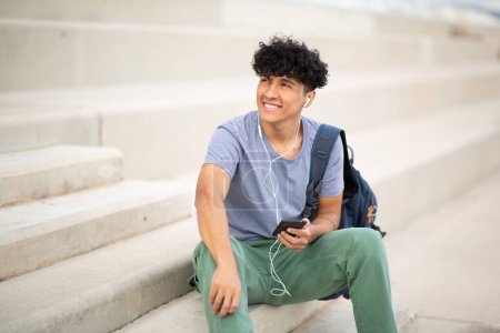 Téléchargez les photos : Portrait jeune homme souriant écoutant de la musique avec écouteurs et téléphone portable - en image libre de droit
