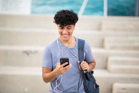 Photo for Portrait smiling young man with earphones looking at mobile phone - Royalty Free Image