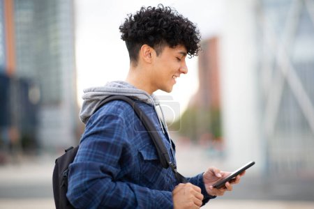 Téléchargez les photos : Portrait latéral jeune homme avec sac et téléphone portable en ville - en image libre de droit