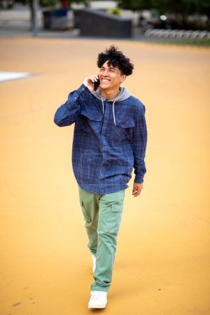 Téléchargez les photos : Portrait complet du corps jeune homme heureux marchant et parlant avec un téléphone portable - en image libre de droit
