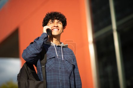 Téléchargez les photos : Portrait jeune homme souriant avec sac parlant sur téléphone portable - en image libre de droit