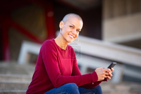 Foto de Retrato de mujer sonriente sentada con teléfono móvil en las manos - Imagen libre de derechos