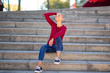 Photo for Full body portrait of female with shaved head siting on steps - Royalty Free Image