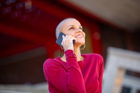 Foto de Retrato de mujer sonriente con la cabeza afeitada hablando con el teléfono móvil - Imagen libre de derechos