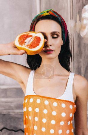 Photo for Beautiful brunette girl with professional make-up holds a grapefruit covering one eye. Advertising poster of environmentally friendly skin care products. Morning beauty routine. Cosmetic care. vitamin - Royalty Free Image