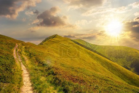 mountain landscape at sunset. traverse path through grassy hillside to the mountain top. beautiful nature scenery with steep slopes in evening light