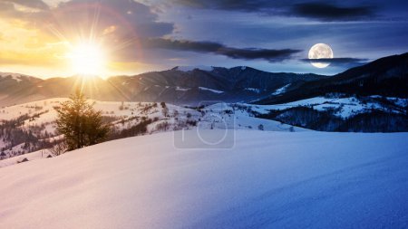 Foto de Paisaje montañoso de invierno en la luz de la mañana. paisaje solsticio con colinas cubiertas de nieve en la distancia debajo de un cielo con sol y luna. concepto de cambio de día y de noche - Imagen libre de derechos