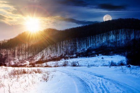 Foto de Paisaje con bosque sin hojas en una colina cubierta de nieve bajo un cielo con sol y luna. invierno solsticio día y noche cambio de concepto - Imagen libre de derechos
