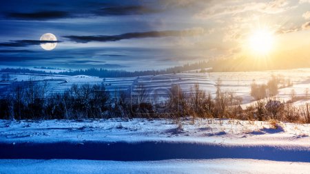 Foto de Paisaje rural en un día de solsticio de invierno. paisaje rural con colinas cubiertas de nieve en la distancia debajo de un cielo con sol y luna. concepto de cambio de día y de noche - Imagen libre de derechos