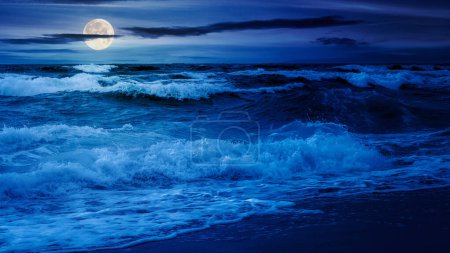 dramatische Seenlandschaft in der Nacht. Wellen krachen im Vollmondlicht auf den Strand