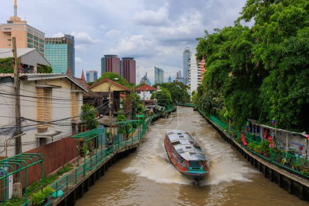 A public transportation boat is in the Phanfa bridge canal (khlong) of Bangkok, Thailand. At the back is the modern city.