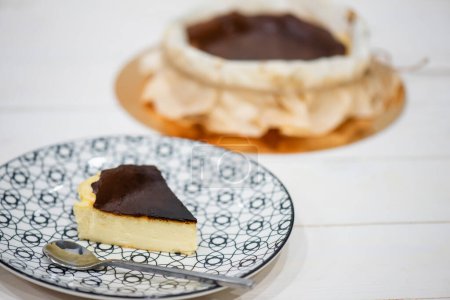 Téléchargez les photos : Piece of cut spanish dessert in dish with blur basque burnt cheesecake on white wooden table - en image libre de droit