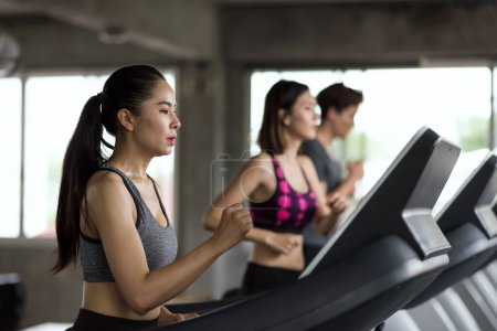 Foto de Grupo de jóvenes amigos asiáticos corren en cintas de correr en el gimnasio deportivo. dos mujeres y un hombre corriendo en la máquina. ejercicio, ejercicio, entrenamiento estilo de vida saludable. - Imagen libre de derechos