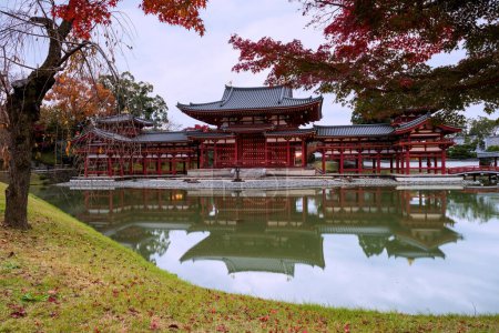 Photo for Byodo-in Buddhist temple,  UNESCO World Heritage Site. Phoenix Hall building with red maple leaf in autumn, Uji city, Kyoto, Japan. Famous travel destination in Kansai. - Royalty Free Image