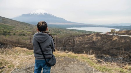 Photo for Rear of young Asian boy with hoodie sweatshirts on top of Yamanakako Panoramadai look at mount Fuji 360 view, Yamanashi, Japan. Famous travel destination at lake Yamanaka. - Royalty Free Image