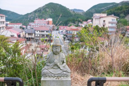 Kleine steinerne Buddha-Statue mit Blick auf die Stadt Unzen onsen vom Unzensan Manmyo Tempel, Nagasaki, Kyushu, Japan. Ariale Architektur und Landschaft.