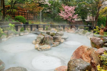 Oniishibozu Jigoku heiße Quelle mit rosa Sakura Blüte des Kirschbaums in Beppu, Oita, Kyushu, Japan.. Stadt ist berühmt für seine Onsen heißen Quellen und 8 große geothermische Hotspots, 8 Höllen von Beppu